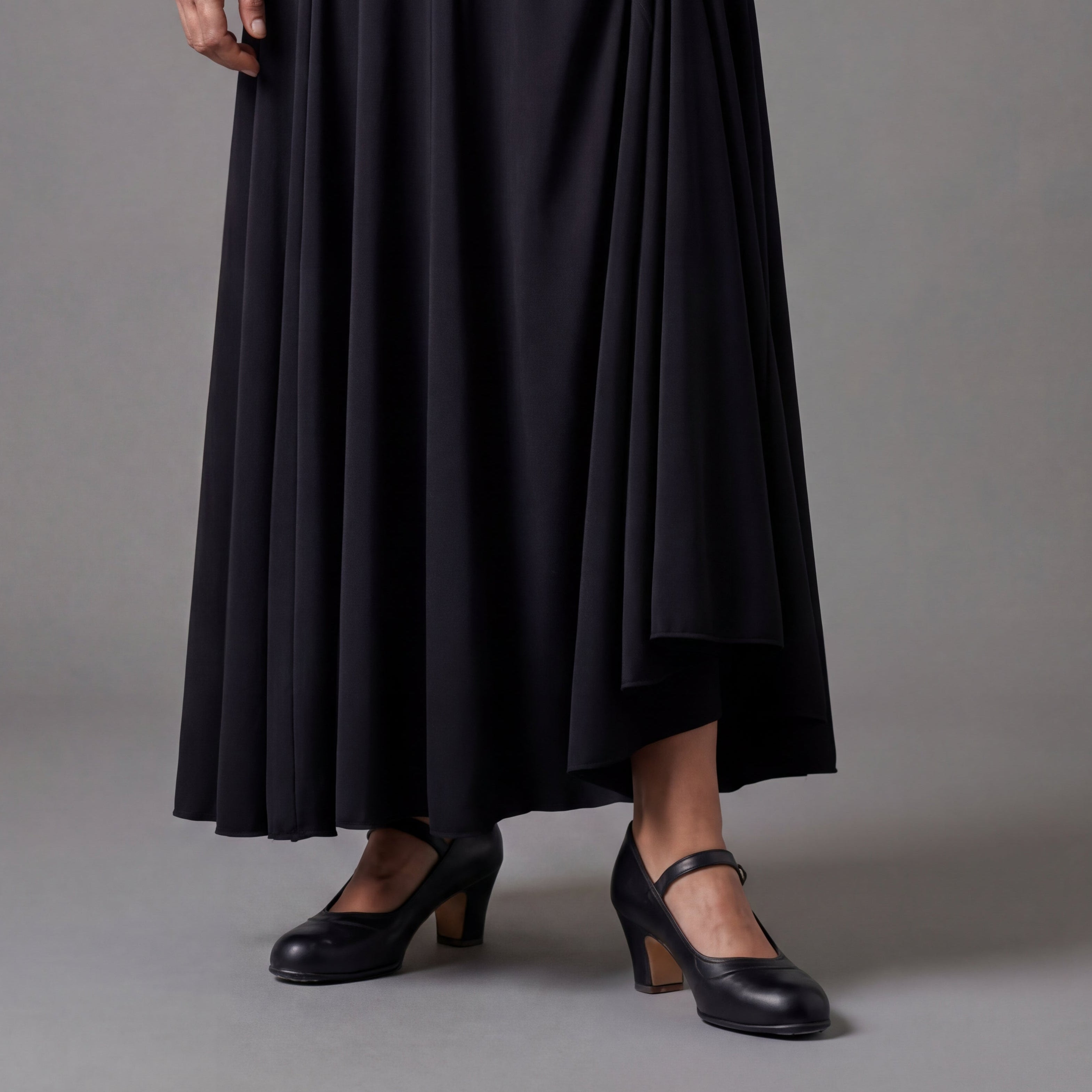 Person wearing a black skirt on a gray background with flamenco shoes with nails